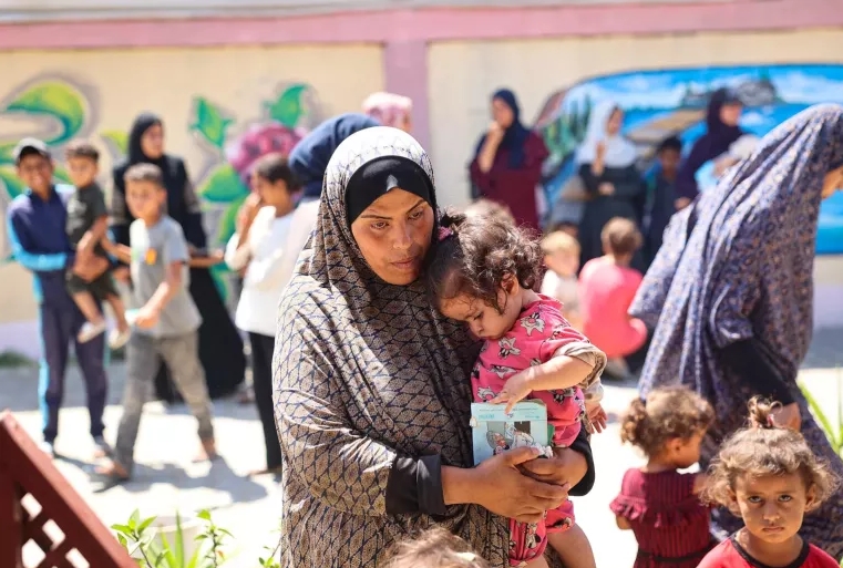UNICEF/UNI601749/El Baba Una mujer alza a su hija mientras esperan durante un examen nutricional en una clínica apoyada por UNICEF en la Franja de Gaza.