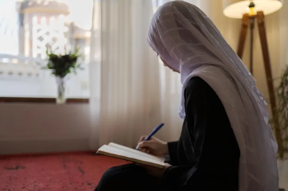 Suraya*, de 18 años, escribe en un cuaderno en su casa en Afganistán. Cuando cursaba 11.º grado, la educación de Suraya se interrumpió abruptamente tras la suspensión de la enseñanza secundaria, una medida que afectó a millones de niñas en Afganistán.